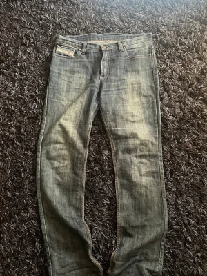Blå raka jeans från Diesel - Snygga blå jeans från Diesel med raka ben och klassisk femficksdesign. Jeansen har slitningar och kontrastsömmar samt en liten Diesel-logga på myntfickan. Perfekta för en avslappnad och trendig stil.
