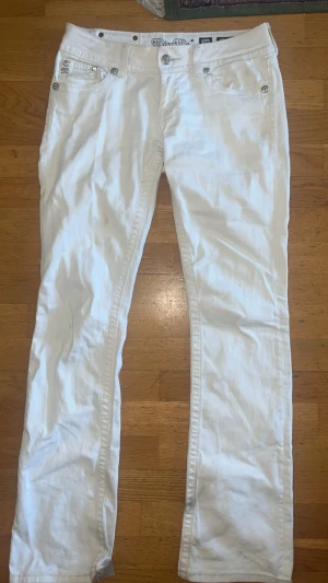 Vita jeans från Miss Me - Säljer ett par vita jeans från Miss Me med utsvängda ben, lågmidjade  och har snygga detaljer på fickorna. Dem har en liten smink fläck vid låret och är lite smutsiga längst ner, går kanske bort i tvätten med vanish men har inte testat då jag inte använder dem längre . 