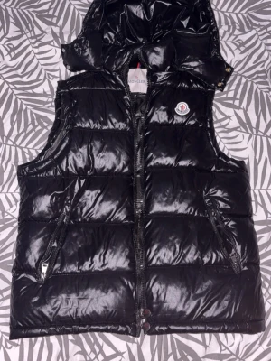Svart Moncler vest  - Svart Moncler vest utan några skador alls, kedjan funkar bra och vestem har inga problem alls Vesten har även bra kvalité och den ser sätt så bra ut. (REP)