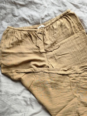 Beige linnebyxor med dragsko - Säljer ett par beige linnebyxor i relaxed fit med elastisk midja och dragsko. Byxorna är tillverkade i en skön linnemix och har en enkel, stilren look som passar perfekt till sommaren. Supersköna och lätta att matcha med olika toppar. Har sytt ett par stygn vid passpoalfickan (se bild).
