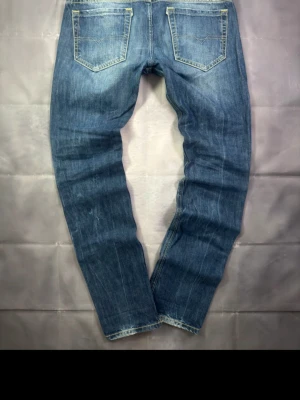 Blå Diesel jeans slitna med raka ben - Säljer ett par blå jeans från Diesel med raka ben och snygga slitningar framtill. Jeansen har klassisk femficksdesign och ljusare partier på låren för en cool, använd look. Perfekta för en avslappnad streetstil.