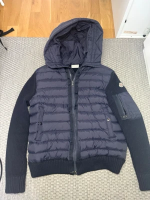 Moncler cardigan marinblå - Säljer en stilren Moncler cardigan i marinblå färg. Cardiganen är i väldigt fint skick utan några defekter och har endast använts ett fåtal gånger. Klassisk och tidlös modell som passar perfekt både till vardags och för en mer uppklädd look. Väldigt skön passform och hög kvalitet som Moncler är känt för.