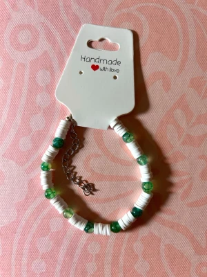 Handgjort armband med vita och gröna pärlor - Snyggt handgjort armband med vita platta pärlor och gröna runda pärlor. Armbandet har en justerbar kedja i silverfärg och passar perfekt för dig som gillar unika accessoarer. Enkel men trendig design som sticker ut.