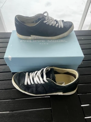 Philippe Model svarta sneakers - Stilrena svarta sneakers från Philippe Model med vita snören och vit sula. Skorna har en klassisk låg design och är tillverkade i läder med diskreta detaljer på sidan och hälen. Perfekta för dig som gillar en clean och tidlös look. Storlek 42 skicket är inte det bästa men dem är självklar äkta