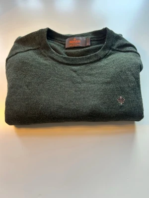 Mörkgrön stickad tröja från Morris - Mörkgrön stickad tröja från Morris med rund halsringning och diskret broderad logga på bröstet. Klassisk modell i mjukt material som passar perfekt till jeans eller chinos.