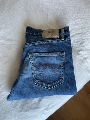 Mörkblå jeans från Edwin - Snygga mörkblå jeans från Edwin med klassisk femficksdesign och raka ben. Jeansen är i bra skick och har en diskret tvättad look och är tillverkade i denim med tydliga sömmar och Pulp Paper-batch bak i midjan. Modell: The Regular Tapered Jeans. Färg: Blue - rinsed. Strl: 32x32 - Jag är 183 cm och väger ca 78 kg. 