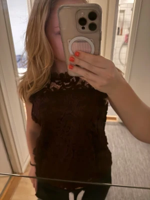 Vinröd spetsblus med hög hals - Säljer en vinröd blus med vacker spets och hög hals. Blusen är ärmlös och har detaljerade broderier över hela tyget. Blusen är i ett bra skick förutom att det saknas två knappar på baktill. Står även att tröjan är i storlek L men jag skulle säga att den är mer som  S/M.