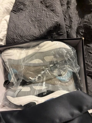 Dior B22 sneakers grå och vit - Säljer ett par Dior B22 sneakers i grått, vitt och ljusblått. Skorna har chunky sula, meshpaneler och detaljer i läder samt textil. Klassisk logga på sidan och cool futuristisk vibe. Kommer i originalkartong med dustbag och kvitto.