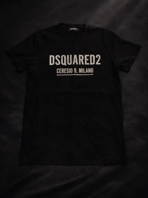 Svart Dsquared2 t-shirt med tryck - Snygg svart t-shirt från Dsquared2 med vitt tryck på bröstet där det står 'DSQUARED2 CERESIO 9, MILANO'. Klassisk passform och rund hals. Perfekt för dig som gillar streetwear och vill ha något stilrent med en exklusiv vibe.