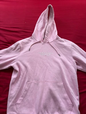Rosa hoodie från Jack & Jones Premium - Säljer en ljusrosa hoodie från Jack & Jones Premium med broderad logga på bröstet. Hoodien har klassisk känguruficka, dragsko i huvan och är gjord i mjukt bomullsmaterial. Perfekt för en chill och avslappnad stil.