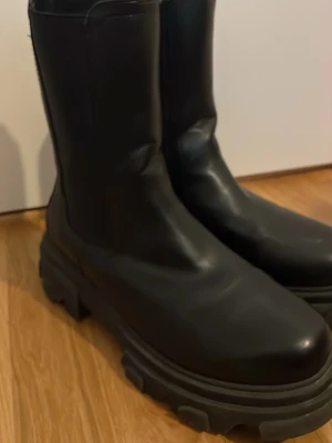 Chunky svarta boots i skinn - Svarta boots med chunky sula och högt skaft. Tillverkade i slätt skinn med rundad tå och grov yttersula för extra edge. Perfekta för dig som gillar en tuffare stil och vill ha boots som sticker ut.