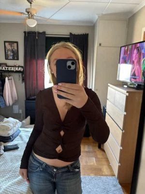 Brun croppad topp med knyt - Säljer en brun långärmad croppad topp med knyt och två öppna detaljer framtill. Toppen har en v-ringad design och sitter tight. Perfekt för dig som vill ha en trendig och snygg look.