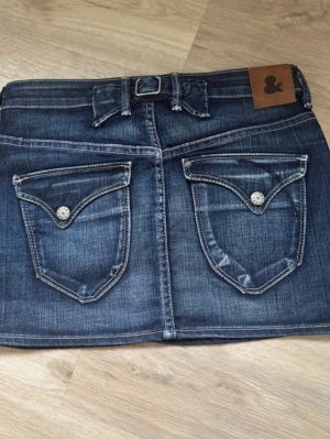 Blå jeanskjol - Snygga blå jeankjol med klassisk femficksdesign och en brun läderpatch vid linningen. Jeansen har kontrastsömmar och är gjorda i denim med en tvättad look. Perfekta för dig som gillar en tidlös och avslappnad stil. Strl 160 men passar mer S