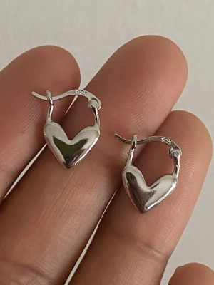 s925 steel Silver pläterat örhängen med hjärtform - Säljer ett par stilrena örhängen i äkta silver med hjärtformad design. De har en blank, polerad yta och smidig klickstängning. Perfekta för dig som gillar minimalistiska smycken med en söt twist.