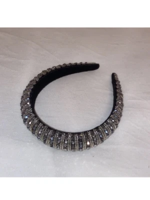 Svart diadem med glittrande stenar - Snyggt svart diadem täckt med glittrande silverfärgade stenar i flera rader. Diademet har en rundad form och ger en lyxig känsla till din look. Perfekt accessoar för att lyfta vilken outfit som helst med extra bling.