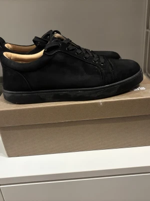 Svarta Loubs - Stilrena svarta sneakers i mocka från Louboutin. Lågt skaft, svarta skosnören och diskret design. Yttersulan är också svart och insidan har en beige ton. Perfekta för dig som gillar minimalistisk och clean stil. I mycket bra skick lite utan några defekter, box ingår. Bara att skriva vid funderingar!