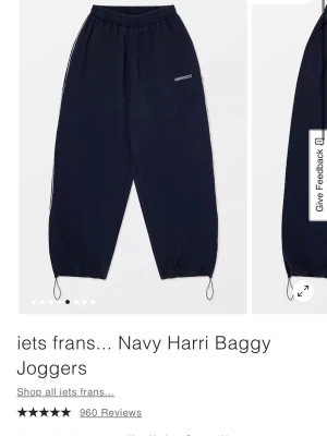Navy Harri Baggy Joggers från Iets Frans - Mörkblå baggy mjukisbyxor från Iets Frans med elastisk midja och justerbara snören vid benslut. Diskret logga på ena benet och vita detaljer längs sidorna. Perfekt för en avslappnad och trendig look.