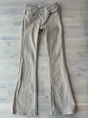 Beiga bootcut jeans från 157 - Snygga beiga bootcut jeans från 157 med låg midja och klassisk femficksdesign. Jeansen har vida ben och är tillverkade i ett mjukt bomullsmaterial. Perfekta för dig som gillar en avslappnad och trendig stil.