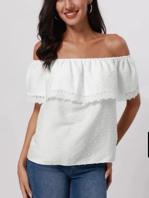 Vit offshoulder topp med spets - Säljer en vit offshoulder topp med bred volang och spetsdetaljer längs kanten. Toppen är ärmlös och har en lätt prickig struktur i tyget. Perfekt för sommaren. Aldrig använt och har lappen kvar
