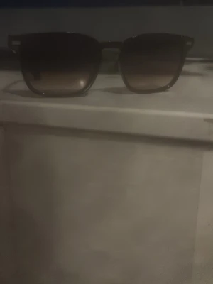 Svart/Brun/Orangea solglasögon med fyrkantig form - Snygga solglasögon med svart båge och fyrkantig form. Glasen är tonade och ger en cool look till alla outfits. Perfekta för soliga dagar och passar till de flesta stilar.