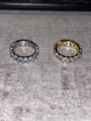 2 riktigt fina ringar i silver och guld  - Säljer två snygga ringar, en i silverfärg och en i guldfärg, båda med gnistrande klara stenar runt hela ringen. Perfekt för dig som gillar att sticka ut och vill ha något extra på fingret. Båda ringar är storlek 9 och säljs för att de inte passar mig. Båda är dessutom helt nya då jag bara använt för att testa 