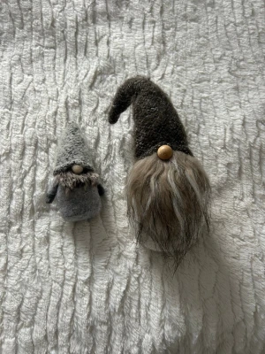 Två grå tomtenissar  - Säljer två dekorativa tomtenissar i grå toner. Den ena har långt skägg och böjd luva, den andra har kortare skägg och rak luva. Båda har träkulor som näsor och mjuka kroppar. Perfekta som juldekoration.