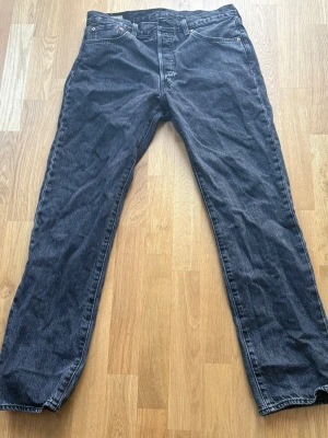 Levi's jeans 501 - Säljer ett par svarta raka jeans från Levi's med klassisk femficksdesign och knappgylf. Jeansen har en mörk tvätt och är tillverkade i kraftig denim. Perfekta för en avslappnad och stilren look.