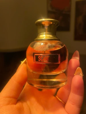 Scandal parfym från Jean Paul Gaultier 30ml - En lyxig parfymflaska från Jean Paul Gaultier, modell Scandal. Flaskan är rund med tjockt glas och har en guldig kork. Vätskan inuti är bärnstensfärgad och etiketten är svart med röd text. Perfekt för dig som gillar exklusiva dofter. 30ml
