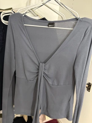 Blå långärmad topp från Gina Tricot - Supersnygg blå långärmad topp från Gina Tricot med v-ringning och knyt framtill. Toppen har en slim passform och är tillverkad i ett mjukt och stretchigt material som känns skönt mot huden. 