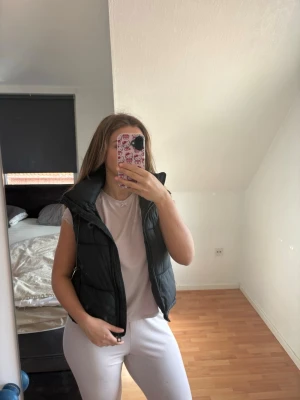 Svart dunväst med hög krage - Säljer en svart dunväst med hög krage och dragkedja framtill. Västen har en klassisk, något figurnära passform och är perfekt att slänga över en hoodie eller t-shirt. Materialet är quiltat och ger en cool look.  Skön vid vårväder men står även emlt kyla till -5 grader. Se defekter sista bilderna. Xs emn passar S. Nypris 400kr.