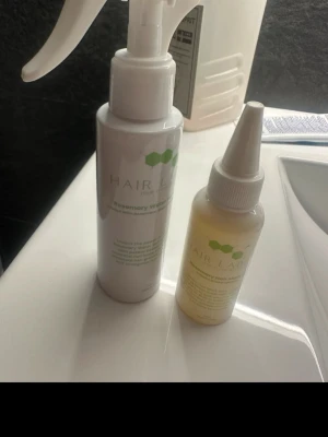 Hair Lab Rosemary hårvårdsprodukter - Två flaskor från Hair Lab, en sprayflaska och en droppflaska, båda med texten Rosemary Water och Rosemary Hair Mist. Flaskorna är vita och genomskinliga med gröna detaljer och används för hårvård. Perfekt för dig som vill boosta håret med rosmarinextrakt.