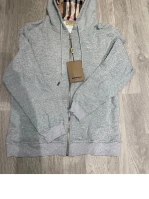 Grå zip-hoodie från Burberry - Helt ny. Skön på insidan. Note att det står L men den sitter som S/M