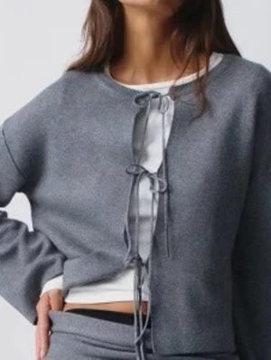 Grå kofta med knytning framtill - Trendig grå kofta med knytning framtill och rund halsringning. Koftan har långa ärmar och är tillverkad i ett mjukt material