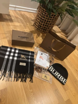 Svart-vit rutig halsduk från Burberry och fin Burberry mössa - Snygg halsduk från Burberry i klassiskt svart och vitt rutmönster med broderad logga och fransar i ändarna. Tillverkad i mjukt material som känns lyxigt och trendigt. Perfekt accessoar för att lyfta din outfit.