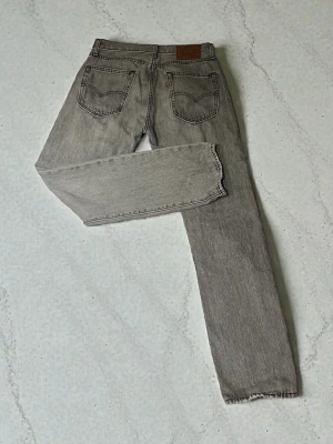 Levi's 551 grå jeans W29 L32 - Grå jeans från Levi's modell 551 med klassisk femficksdesign och raka ben. Jeansen har dragkedja och knappstängning, samt detaljerad läderpatch bak i midjan. Materialet är slitstark bomullsdenim med Water<Less-teknologi. Jeansen är i mycket bra skick.