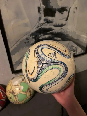 Adidas fotboll Brazuca design - Säljer en Adidas fotboll med klassisk Brazuca-design i vitt med blå, gröna och orange detaljer. Bollen har en rund form och är tillverkad i syntetmaterial, perfekt för matcher och träning på planen. Kanske inte bästa skicket men fin att sätta som dekoration. Vm bollen från 2014 så den har 12 år på sig därför priset kanske är lite högt. Bra till samlare. Skickas opumpad men såklart kan man pumpa den själv