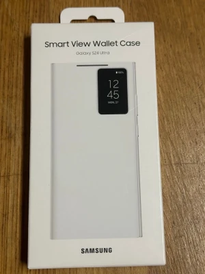 Samsung Smart View Wallet Case S24 Ultra - Snyggt och praktiskt vitt plånboksfodral till Samsung Galaxy S24 Ultra. Fodralet har smart fönsterfunktion som visar tid och aviseringar utan att öppna locket. Perfekt för dig som vill ha både skydd och stil i ett.