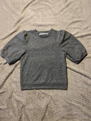 Grå puffärmströja  - Mysig grå tröja med puffärmar och rund halsringning. Tröjan har en rak passform och är gjord i ett mjukt, stickat material som känns skönt mot huden. Mått: Längd 54cm, Bredd mellan armarna 45cm, Bredd nertill 40cm. Material: 95% polyester, 5% elastan.