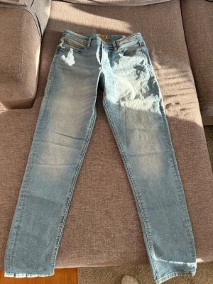 Ljusblå jeans från Jack & Jones - Säljer ett par ljusblå jeans från Jack & Jones i storlek 170. Jeansen har en slim fit-modell med slitningar och tvättade detaljer framtill. Klassisk femficksdesign och knappgylf. Perfekta för en avslappnad och trendig look.