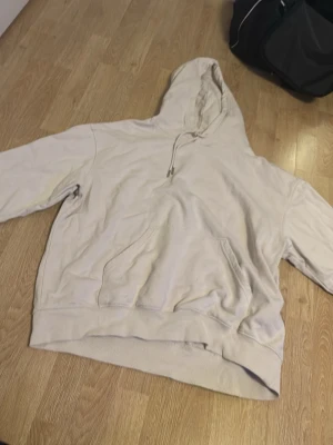 Beige hoodie med huva och ficka - En basic beige hoodie med huva och stor magficka. Hoodien har dragsko vid huvan och ribbade muddar vid ärmslut och nederkant. Perfekt för en avslappnad och chill stil. Materialet känns mjukt och skönt mot huden.
