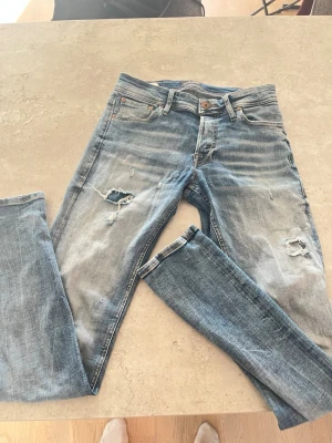 Jack & Jones  - Jag säljer ett par blåa grish Jack and Jones jeans med slitningar och blekta. Jeansen är stiliga, sofistikerade och i bra skick. Ny pris 799kr