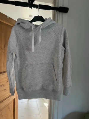 Grå hoodie från Russedress, skicka 10/10 knabbt använd  - Snygg ljusgrå hoodie från Russedress med vit dragsko i hatsan och stor magficka framtill. Tillverkad i mjukC bomullsblandning och har logga tryckt på ärmen. Perfekt för chill dagar och enkel att matcha med jeans eller sop.