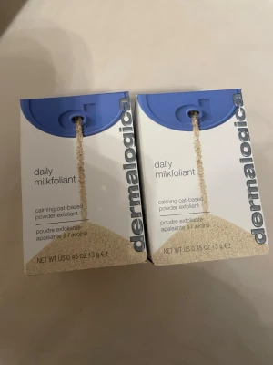 Dermalogica Daily Milkfoliant exfoliant 2x 13g - Två förpackningar Dermalogica Daily Milkfoliant, en lugnande exfolierande pulverprodukt baserad på havre. Förpackningarna är vita med blått lock och silverdetaljer. Perfekt för dig som vill ha en mild exfoliering i din hudvårdsrutin.