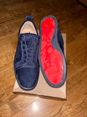Christian Louboutin - Snygga mörkblå sneakers från Christian Louboutin i mocka med klassisk röd sula. Skorna har rund tå, matchande mörkblå snörning och diskreta sömdetaljer. Perfekta för dig som vill sticka ut med exklusiv design och ikonisk färgkombination.