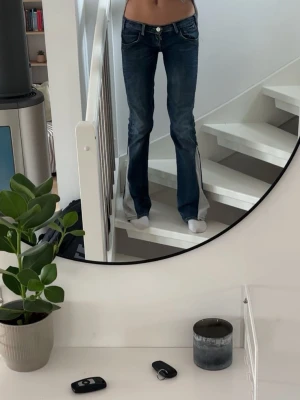 Mörkblå bootcut jeans med låg midja - Snygga mörkblå bootcut jeans med låg midja och klassiska fem fickor. Jeansen har en lätt tvättad look och vida ben nertill. Perfekta för en trendig och avslappnad stil.