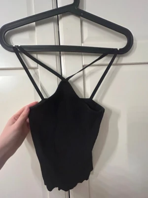 Svart ribbad linnetopp Vero Moda - Säljer en svart ribbad linnetopp från Vero Moda i storlek XS. Toppen har smala axelband som korsas framtill och en croppad passform. 