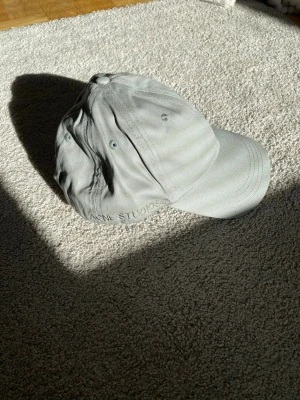 Ljusgrå keps från Acne Studios - Snygg ljusgrå keps från Acne Studios med broderad logga på sidan. Klassisk böjd skärm och justerbar rem bak. Tillverkad i bomull för en clean och stilren look. Perfekt accessoar för att lyfta din outfit.