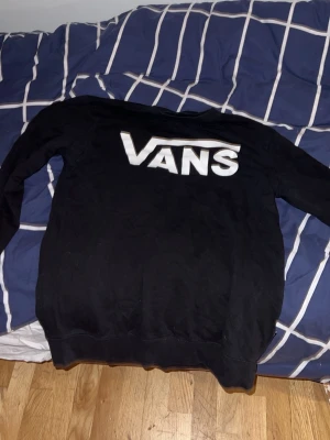 Svart sweatshirt från Vans - Säljer en svart sweatshirt från Vans med stort vitt Vans-tryck på ryggen. Tröjan har rund halsringning och långa ärmar. Perfekt för dig som gillar streetwear och vill ha en enkel men snygg tröja. 