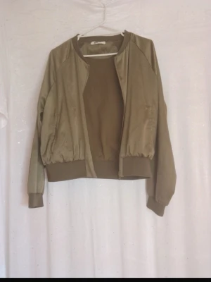 Olivgrön bomberjacka med ribbade muddar - Andas cool stil med denna olivgröna bomberjacka. Jackan har soprena lin charm, ribbade muddar och midja samt sopren dragkedja framtill. Materialet är mj, troligtvis polyester eller bomulls recon, och jackan har en klassisk bomberpassform. Har e. Liten fläck vid dragkedjan men det är inget man tänker på!