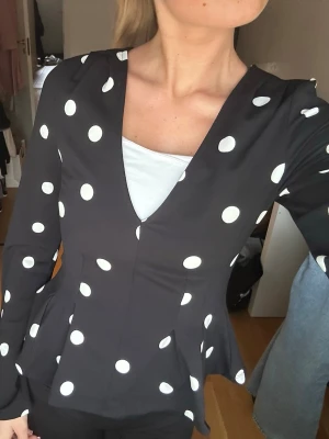 Svart prickig blus med v-ringning - Snygg svart blus med vita stora prickar och v-ringad hals. OBS jag har ett vitt linne under , tröjan är alltså bara det pricka och de vita hör ej ihop